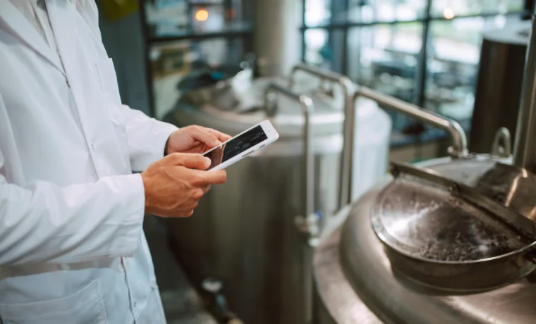 Lebensmitteltechnologe erfasst Produktspezifikationen am Tablet vor Prozesstanks